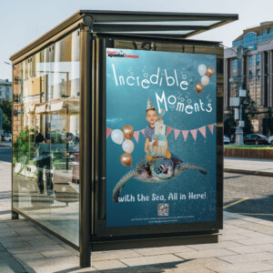 An outdoor advertisement displayed in a bus shelter featuring a poster for 'Aquarium Canada'. The poster shows a joyful child riding on the back of a sea turtle under the sea, surrounded by bubbles and with party balloons tied to the turtle. Above the child, the text 'Incredible Moments' is written in a playful font. Below the child, it reads 'with the Sea, All in Here!' indicating an immersive experience at the aquarium. A QR code and additional text are at the bottom of the poster, presumably for more information or tickets. The bus shelter is on a city street with buildings and reflections visible in the glass.